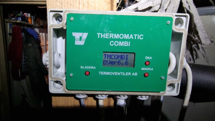 Grön styrenhet för värme, märkt "THERMOMATIC COMBI", knappar "ÖKA" och "MINSKA", kablar, rörbakgrund.