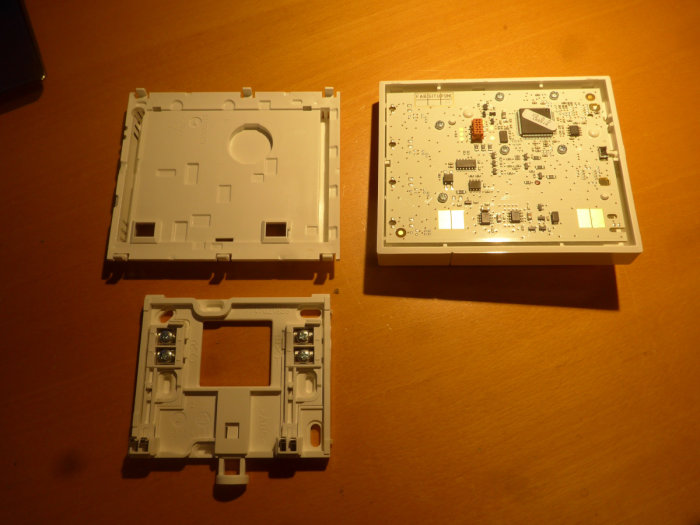 Öppnad elektronisk enhet med kretskort och plasthölje på träbord, skruvar synliga, inomhusbelysning.