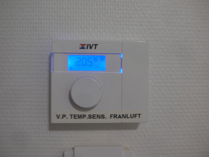 Digital termostat på vit vägg visar 20.5°C. Svensk text "V.P. TEMP. SENS. FRÅNLUFT". Märke IVT.