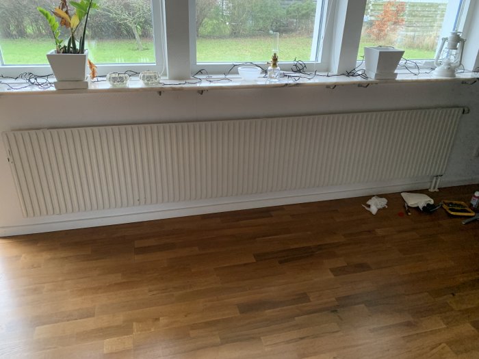 Inomhusrum med ett fönster, element, golv i trä, dekorationer på fönsterbrädan och några leksaker på golvet.