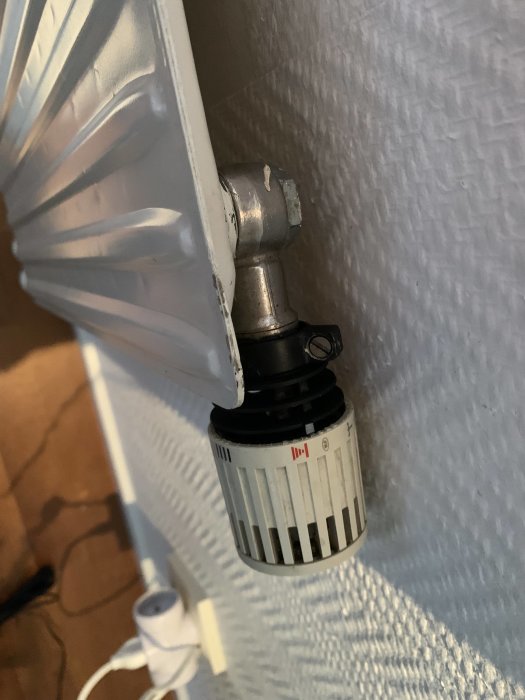 Element i ett rum med termostatventil, vit radiator, vägg, delvis synlig golv.