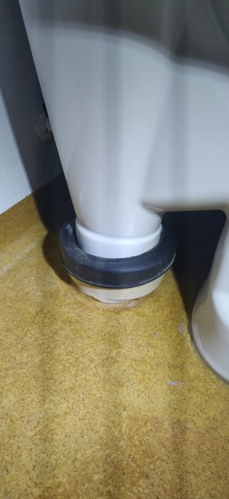 Närbild på toalettens bas med tätning mot gult kakelgolv.