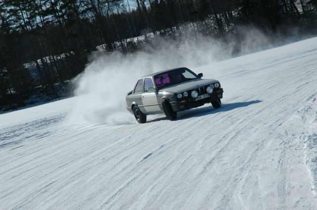 Bil driver i snö, skapar snötäcke, dynamisk rörelse, klarblå himmel, vinterdag, fritidsaktivitet.