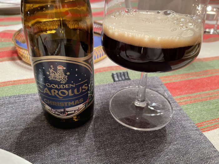 En julölflaska märkt "Gouden Carolus Christmas" intill ett glas mörk öl med skum.