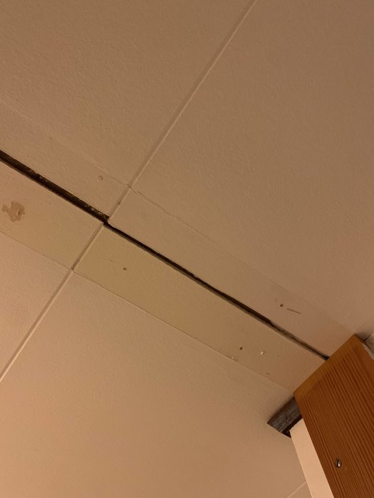 Vit tak med synlig balk, fläckar och gul dörrkarm i ett hörn.