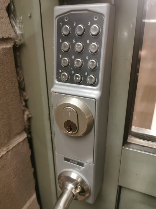 Elektronisk kodlås och nyckellås på en dörr, nummerknappar, säkerhetsåtgärd, grå metall, ingångskontroll.