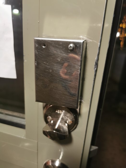 Metallknappsats och låscylinder på dörr, med spegelbild och några spindelnät.