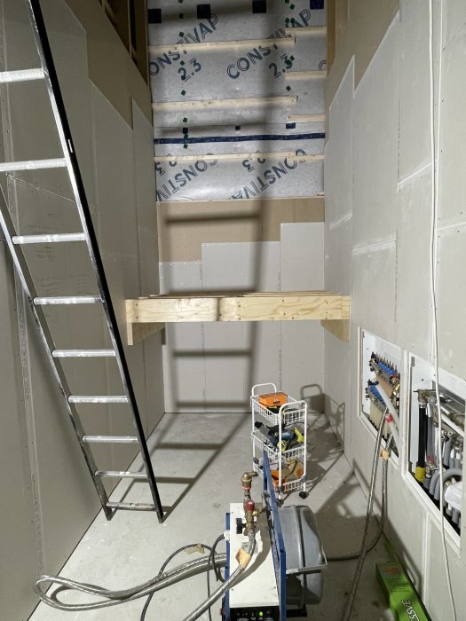 Trappa i pågående konstruktion, isoleringsmaterial, verktyg, byggmaterial, gråa väggar, arbetsbelysning, stege, avstängningsventil.