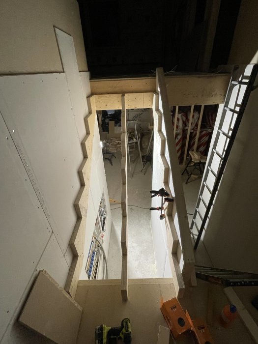 Under uppbyggnad: trätrappa inomhus, platsbyggd, verktyg och konstruktionmaterial synliga, oavslutad installation.