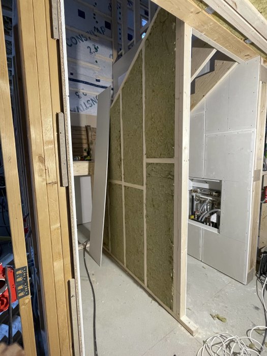 Byggarbetsplats inomhus, isolering i väggar, träreglar, gipsplattor, rörledningar synliga, oavslutat byggprojekt.