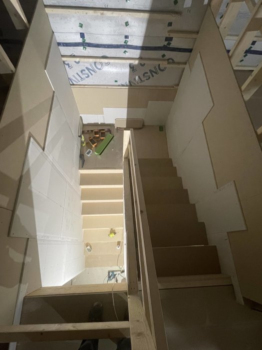 Trappa under konstruktion inomhus med verktyg och byggmaterial synliga. Oavslutade väggar och isolering.