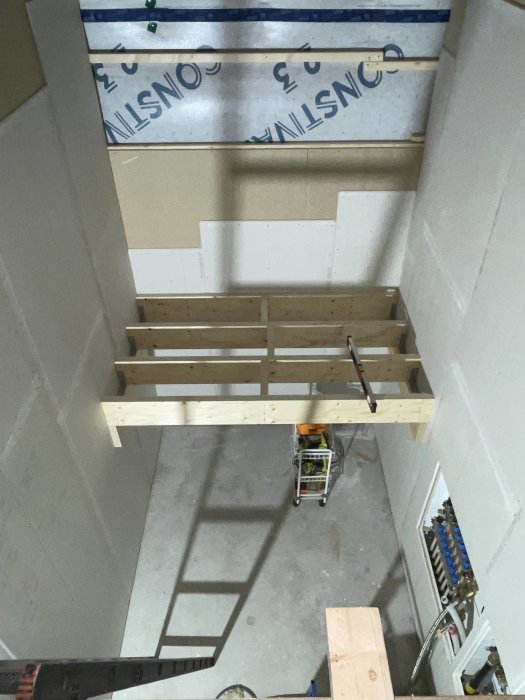 Utsikt ovanifrån på ett underkonstruktionsarbete i ett tomt rum med verktyg synliga.