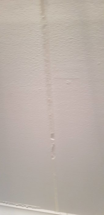 En vit vägg med en synlig vertikal skada och några märken eller fläckar.