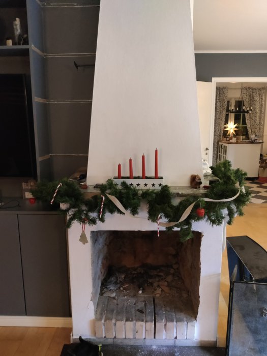 Öppen spis med juldekorationer och röda ljus i ett vardagsrum.