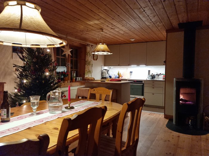 Mysig, hemtrevlig stuga med julgran, brinnande vedspis, dukat matbord och kök.