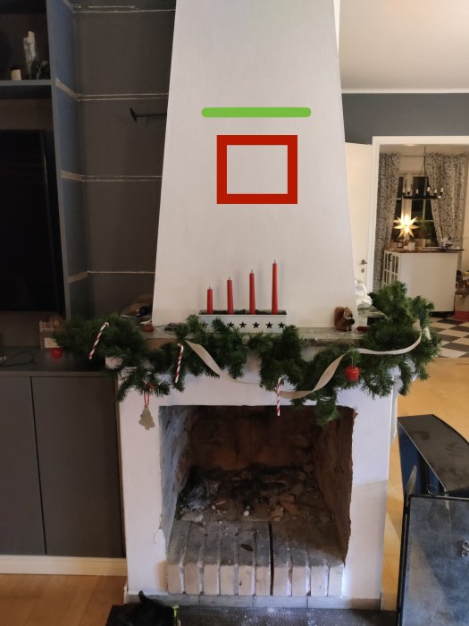 En kakelugn dekorerad med julgransgirlanger och röda ljus; interiör med julstämning.