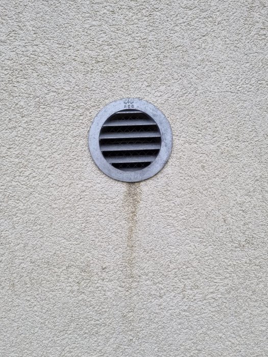 Rund ventilation på en grå putsad vägg med synliga smutsspår strömmande nedåt.