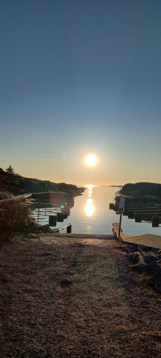 Solnedgång över stilla hav vid brygga, klar himmel, reflexion i vatten, klippor och natur.