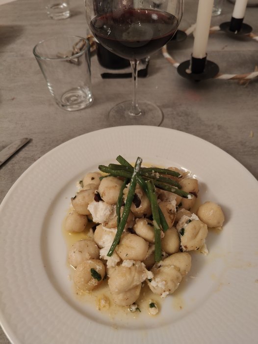 Gnocchi med gröna bönor och ost, vin, middagsbord med ljusstakar, mysig atmosfär.