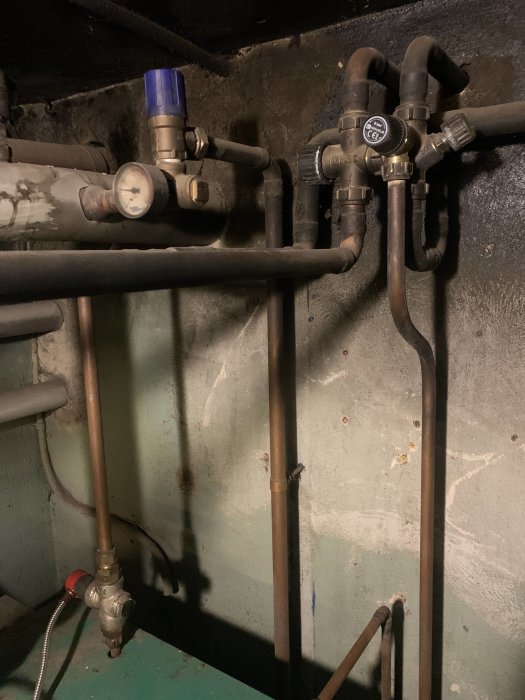 Rörledningar, mätare och ventiler i ett mörkt, gammalt pannrum eller utrymme.
