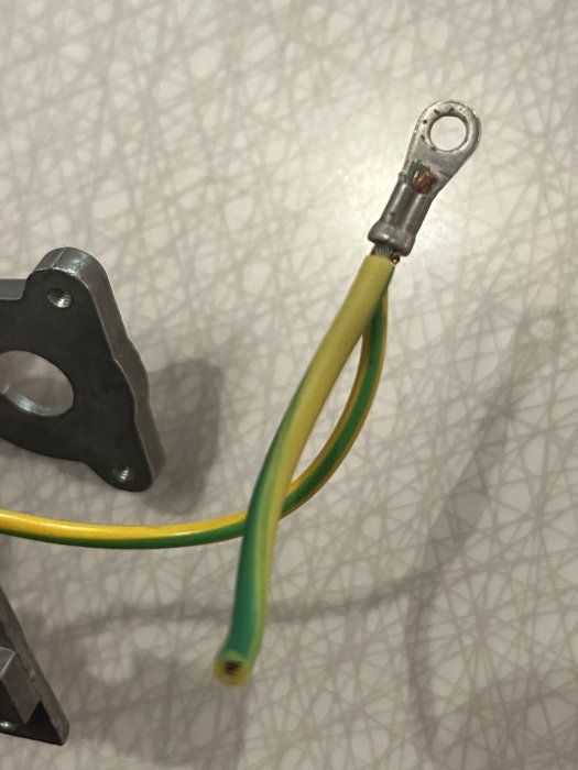 Elektrisk kabel med gult och grönt omslag, kringkopplingsbleck, på mönstrad bakgrund.