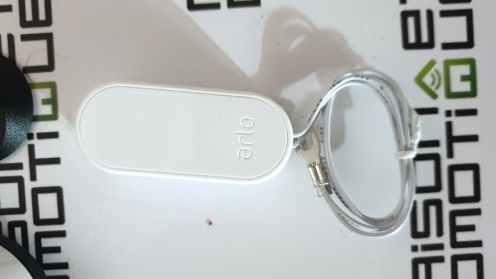 Ett vitt, ovalt föremål med text, kopplat till en USB-kabel, på ett mönstrat underlag.