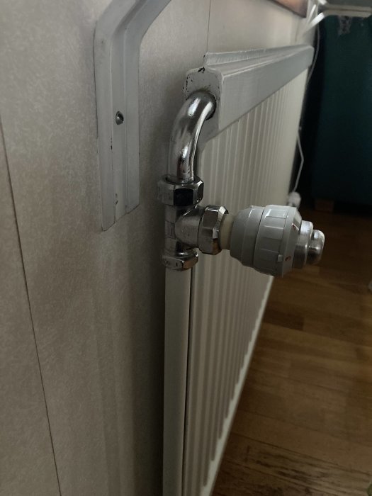 Radiator med termostatventil, vit väggfäste, reflekterande kromad detajl, inomhusmiljö, trägolv.