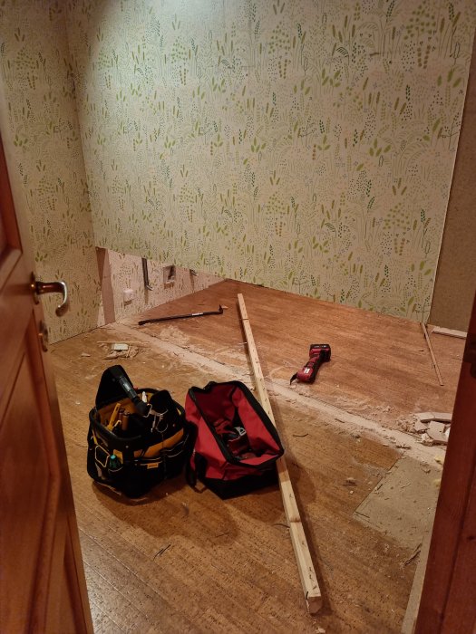 Renoveringsarbete pågår, verktygsväska, ryggsäck och borr på ett tomt golv med tapetväggar.