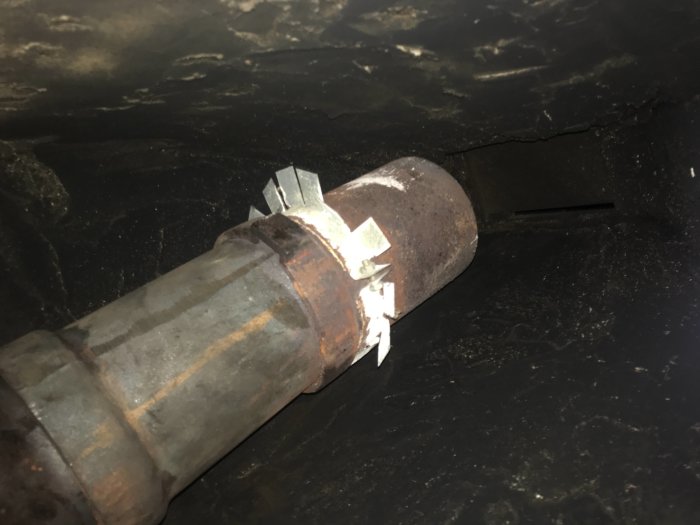 Rörledning med fixeringsklämmor i en mörk utrymme, möjlig underjordisk eller industrianläggning.