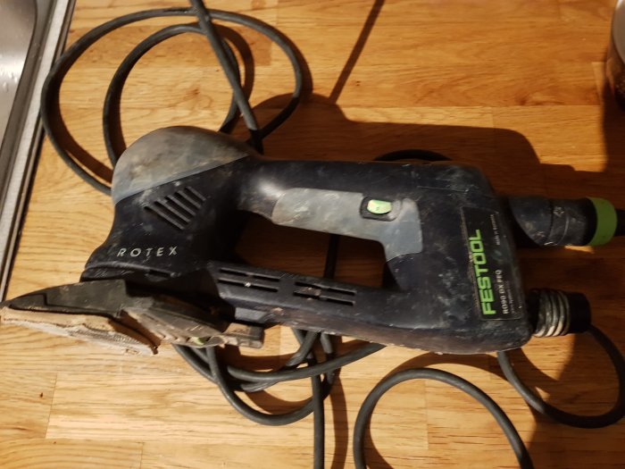 Festool Rotex slipmaskin, använd och smutsig, på ett trägolv, elektrisk sladd i bakgrunden.