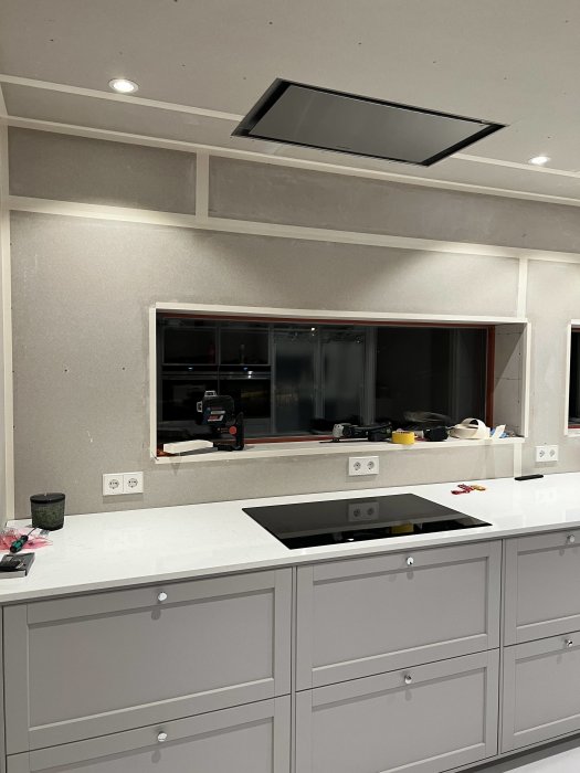 Modernt kök under renovering, bänkskåp, inbyggd häll, spegelbakgrund, belysning ovanför, arbetsmaterial synliga.
