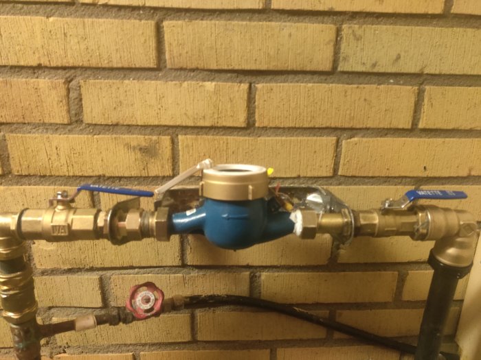 Vattenmätare och ventiler mot tegelvägg. Rörledningar med blå och röd kran. Installation, VVS, infrastruktur.