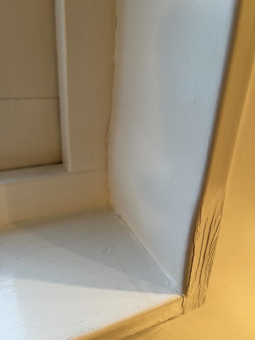 Vit hörn av ett rum med skuggor, paneler och lister, naturligt ljus, detaljbild av interiör.