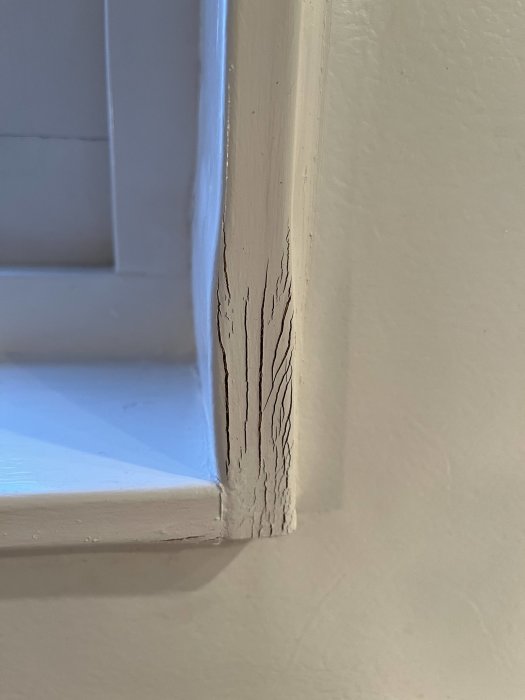 Vitt fönsterkarm med sprickor i färgen, närbild med en del av fönsterrutan synlig.