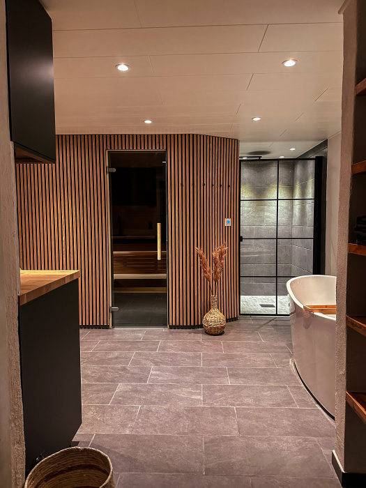 Modernt badrum med träpaneler, badkar, duschkabin och bastu. Stilfull inredning och grått golv.