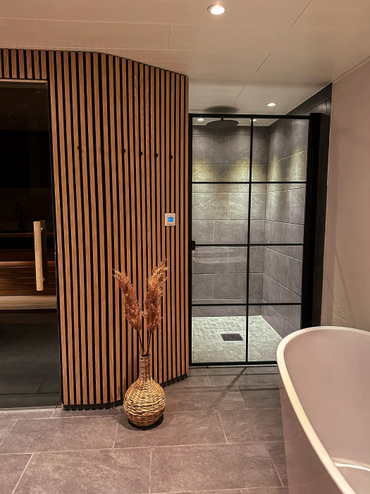 Modernt badrum med snygg inredning, trävägg, badkar, dusch och dekoration av torkade växter.