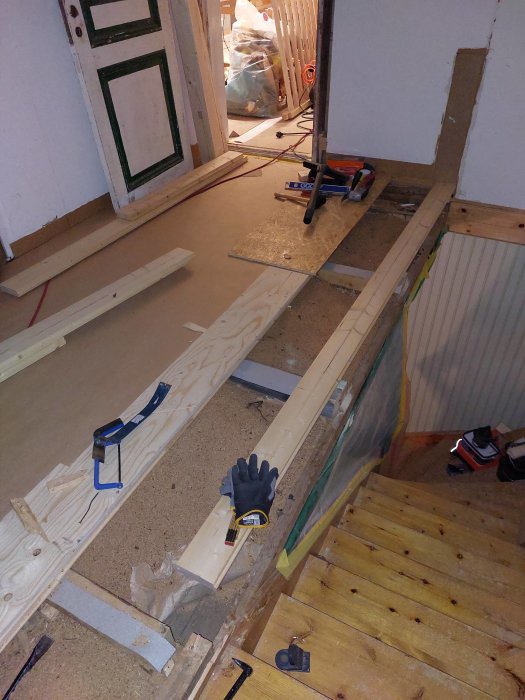 Byggarbetsplats inomhus, trämaterial, verktyg, handske, pågående renovering eller konstruktion, oorganiserat, trätrapp.