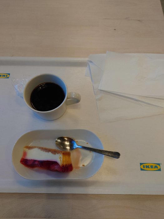 Ett kaffekopp och en nästan uppäten bakelse på en bricka med IKEA-logotyp.