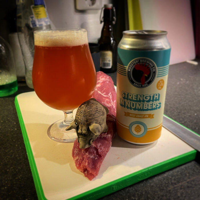 Ölglas med skum, IPA burk, skärbräda, köttbit, elefantfigurin på köksbänk.
