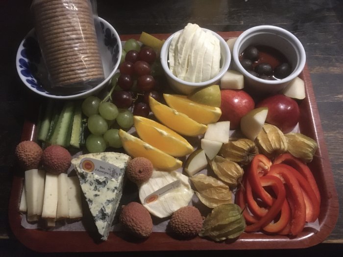 Ett serveringsfat med ostar, kex, frukt och grönsaker för snacks eller mingel.