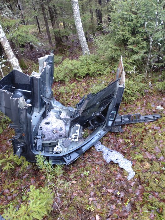 Ödelagd elektronikdel i skogsmiljö, trasig plast och metall, förfallet på skogsmark, tekniskt avfall, naturen tar över.