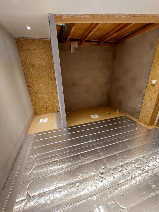 Rum under renovering med isolering på golvet och oskyddade träbjälkar i taket.