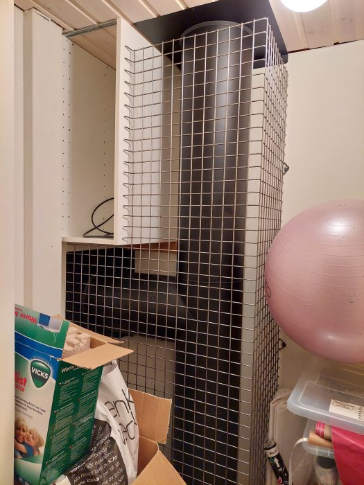 Cluttered storage closet with items, shelving unit, wire grid, pilates ball, boxes, and a dark corner.