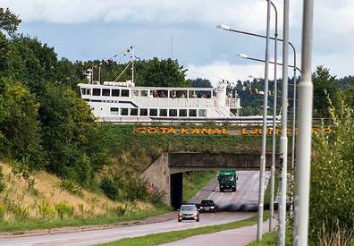 Ett vitt fartyg ovanpå en bro över en väg med texten "Göta kanal" där bilar kör under.