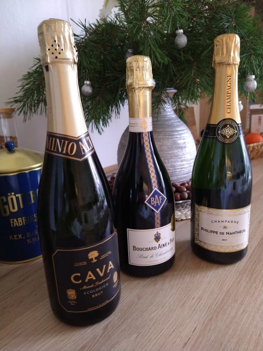 Tre flaskor mousserande vin med granris och juldekorationer i bakgrunden, festlig stämning.