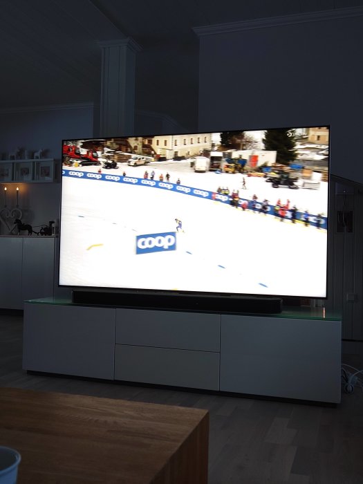 TV-skärm visar längdskidåkning i vardagsrum, tävlingsscenen, möbler i förgrunden, inomhus.