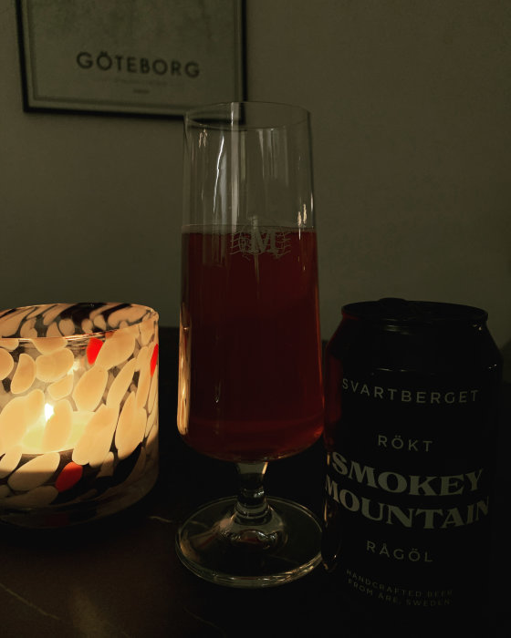 Ölglas med röd vätska, burk med text, ljus i mosaiklykta, tavla "Göteborg". Mörk atmosfär.