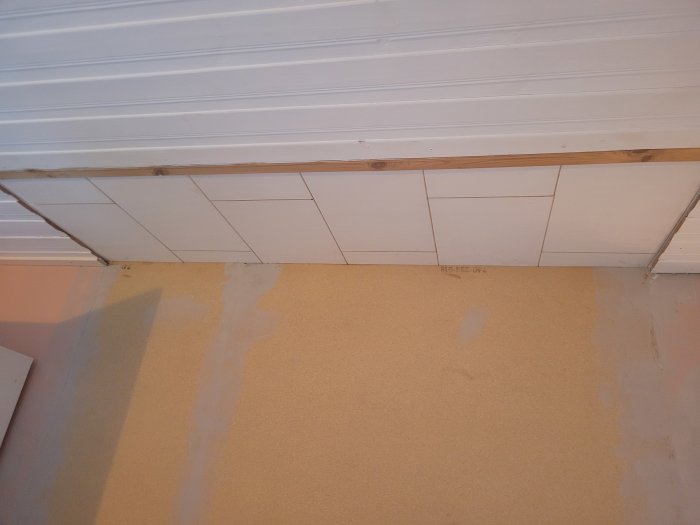 Oavslutat innertak med synliga reglar, vit panel, spacklade väggar redo för målning. Renovering pågår.