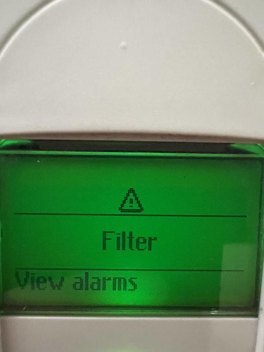 Digital display visar varningssymbol, orden "Filter" och "View alarms", grön bakgrundsbelysning, del av apparat.