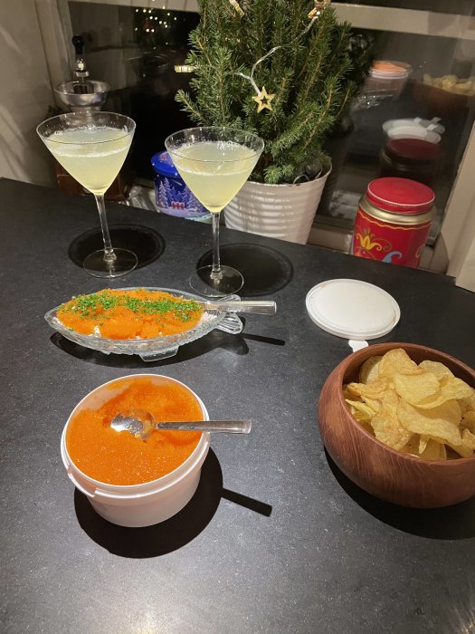 Två cocktails, kaviar på bröd, tomatsoppa och chips, köksbänk, juldekorationer i bakgrunden.